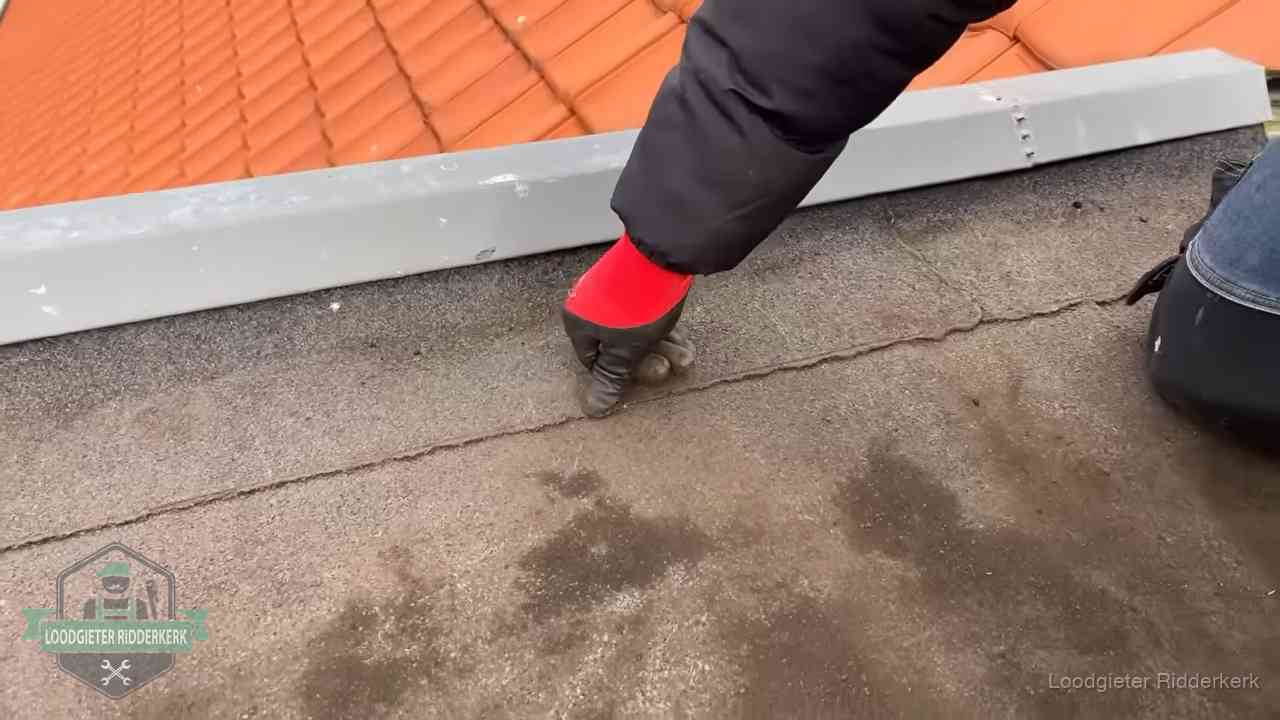 Vakman wijst een naad met vochtplekken aan op een bitumen plat dak in Ridderkerk