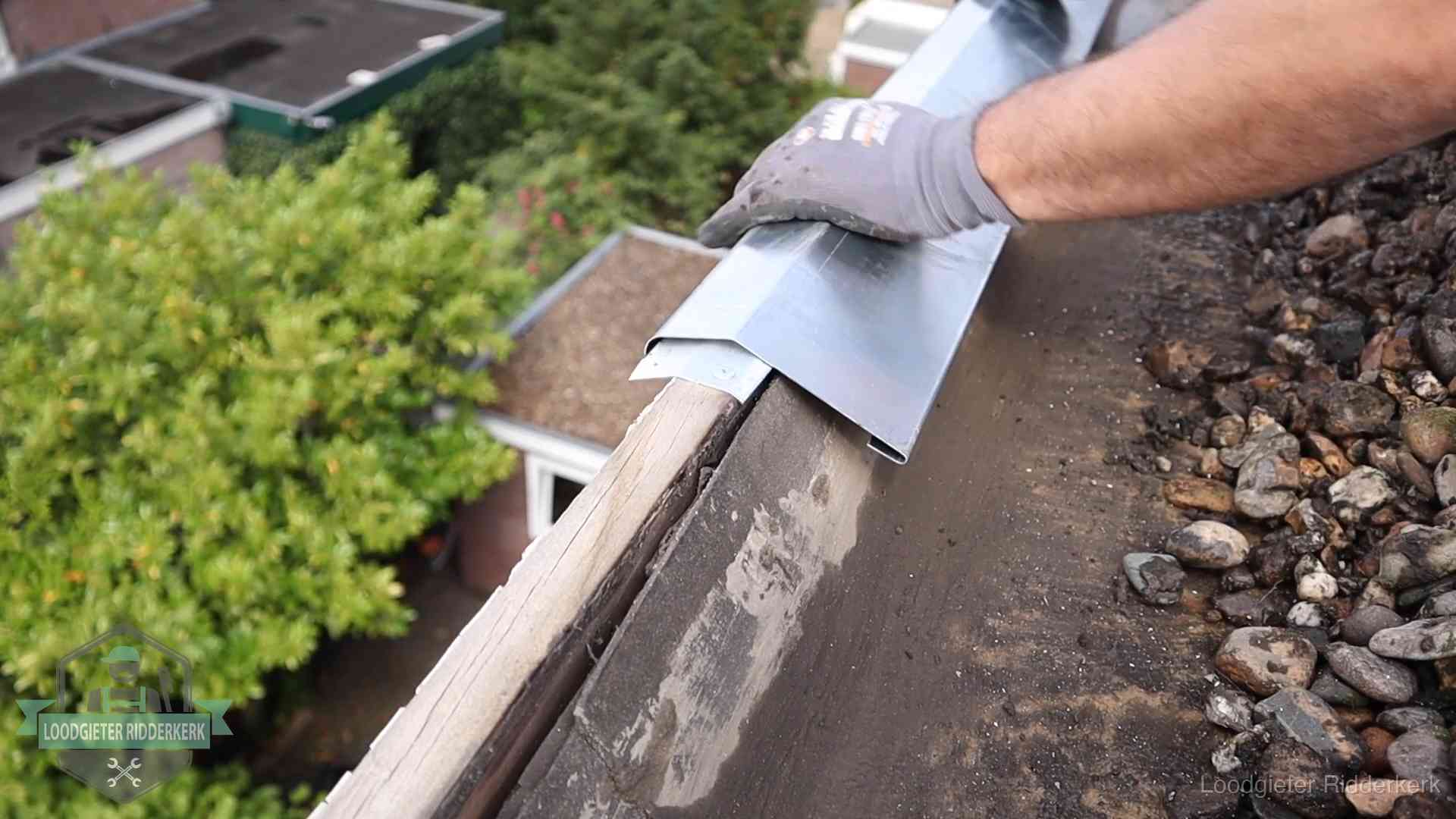 Dakdekker plaatst een zinken deklijst op een dakrand met uitzicht over een woonwijk in Ridderkerk