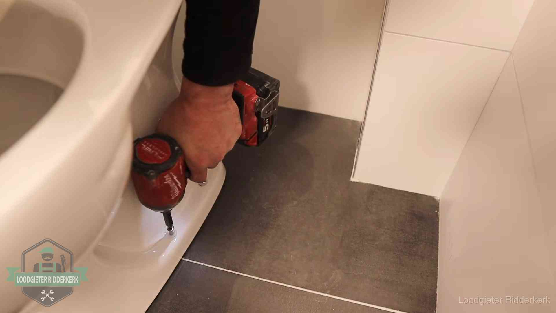Loodgieter zet de voet van een wc-pot vast op de tegelvloer in Ridderkerk